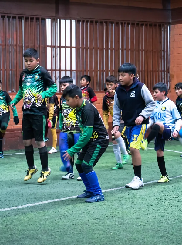 Niños entrenando conducción del balón en cancha techada